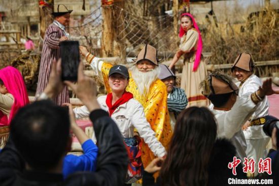 游客和罗布人村寨景区里的人一起跳舞。　庞博 摄