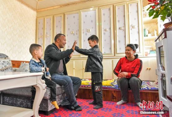 4月17日，新疆喀什地区莎车县易地搬迁安置新区，伊敏江·塔什与姑丽扎尔·木海拜提（右）夫妇在家中陪孩子游戏。